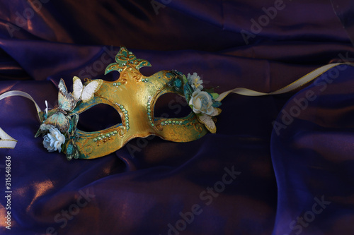 Photo of elegant and delicate gold Venetian mask over purple silk background