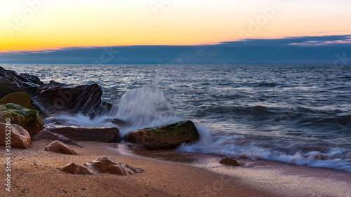 Wave crashing on the rocky seashore at sunset time