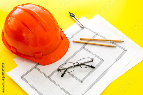 Builder helmet and blueprints on yellow background