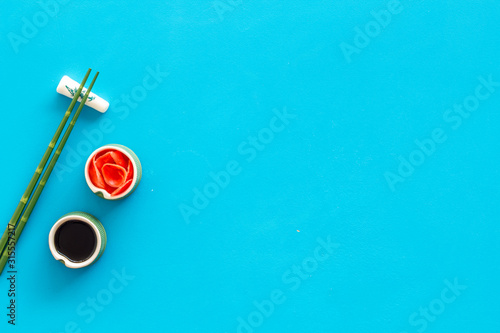 Set of chopsticks for sushi, ginger and soy sause on blue background top-down frame copy space