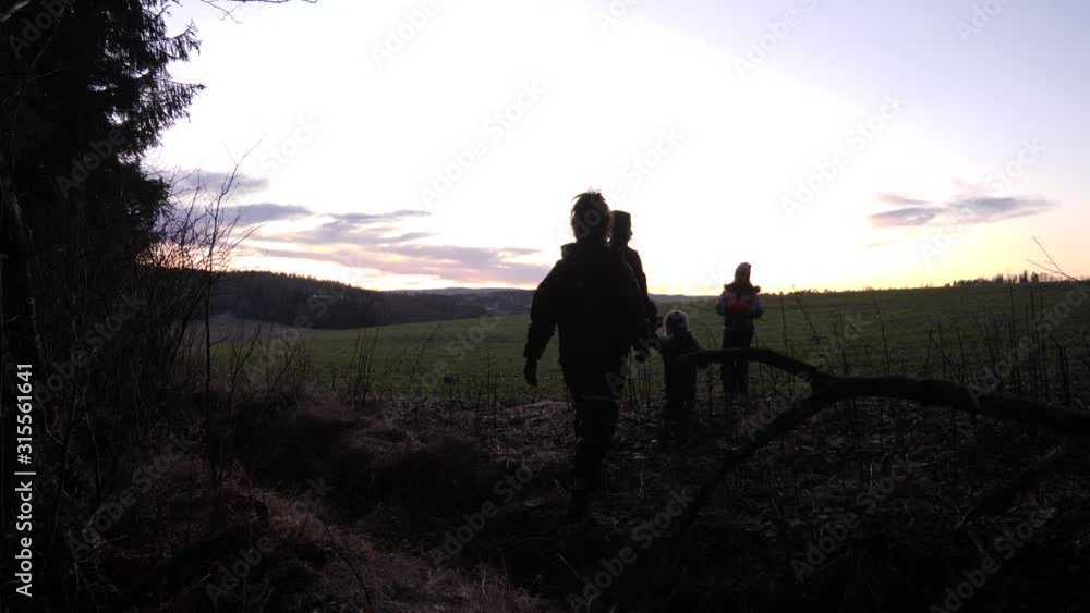 Family with two young children on a hike walks out of the forest and into a field as the sun is setting - people are in silhouette Family with two young children on a hike walks out of the forest and into a field as the sun is setting - people are in silhouette