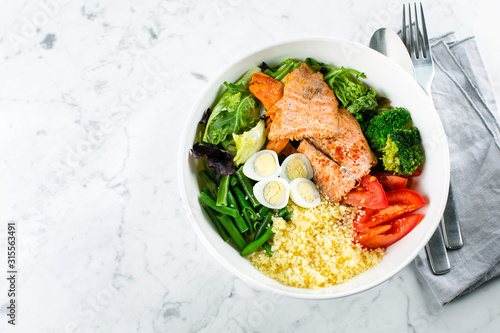 Healthy meal, keto food concept. Fish salad bowl on marble table background. Salad with salmon, couscous, vegetables, quail eggs. Top view, copy space