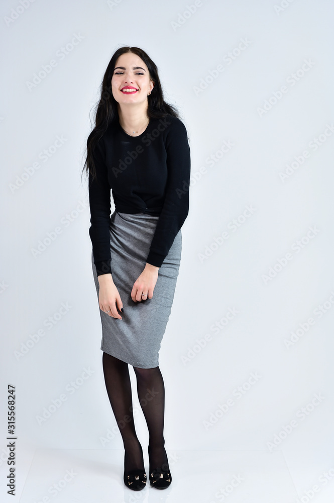 Concept of business female photo portrait. A brunette girl with a smile with long hair with excellent makeup in a gray dress on a white background stands right in different poses in full growth. Concept of business female photo portrait. A brunette girl with a smile with long hair with excellent makeup in a gray dress on a white background stands right in different poses in full growth.