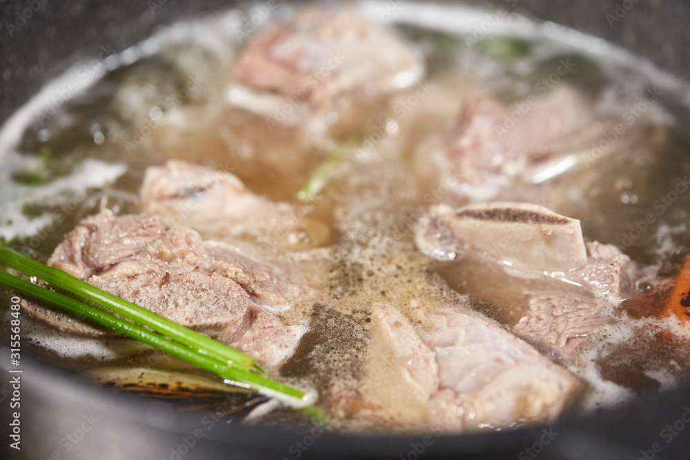 Traditional beef broth with vegetable, bones and ingredients in pot, cooking recipe. Soup in a cooking pot with ladle on dark stone background. Top view Traditional beef broth with vegetable, bones and ingredients in pot, cooking recipe. Soup in a cooking pot with ladle on dark stone background. Top view