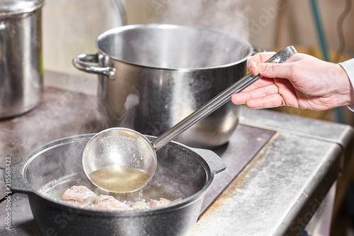 chef cook adds the ingredients. traditional beef broth with vegetable, bones and ingredients in pot, cooking recipe. Soup in a cooking pot with ladle on dark stone background. Top view