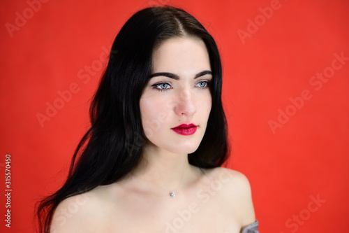 The concept of a glamorous female portrait. Portrait of a brunette girl with a smile with long hair with excellent makeup on a red background in various poses.