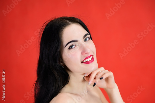 The concept of a glamorous female portrait. Portrait of a brunette girl with a smile with long hair with excellent makeup on a red background in different poses side view.