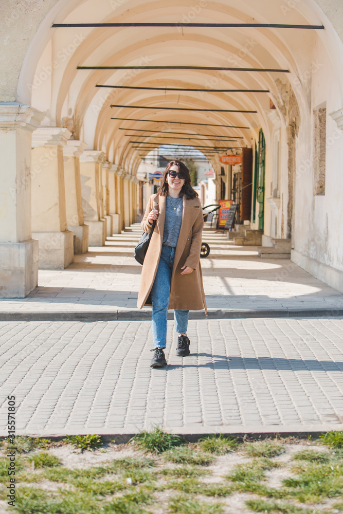 young pretty fashionable woman walking in brown coat by street