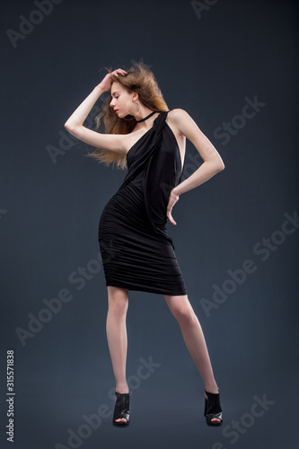 Young beautiful girl model in black dress in Studio on dark background