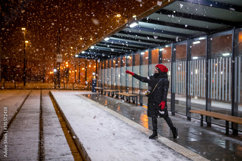 woman looking at snow standing at tram station winter night