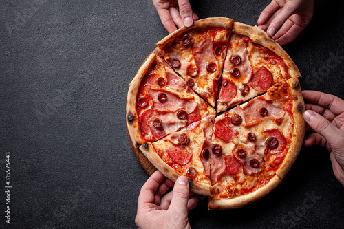 Italian Cuisine. Pepperoni pizza with salami sausage and red hot pepper, lies on a wooden board, on a black background. background image, copy space text