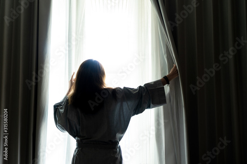 Beautiful woman is opening the curtain at the window in the morning.