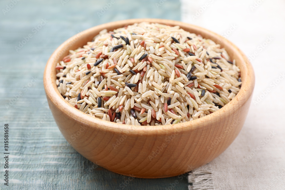 Mix of different brown rice in bowl on light blue wooden table Mix of different brown rice in bowl on light blue wooden table