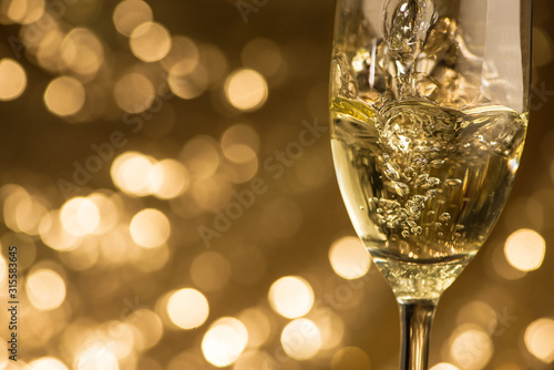 Sparkling white champagne is poured into a glass on a golden bokeh circles background