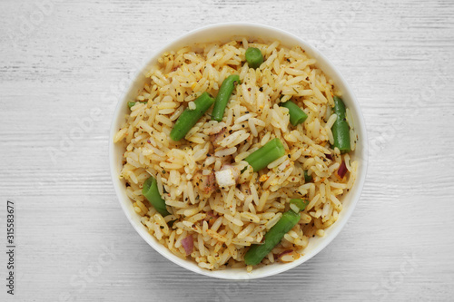 Tasty rice pilaf with vegetables on white wooden table, top view