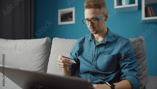 Casual young man doing online purchase by credit card using laptop staying home © MYDAYcontent