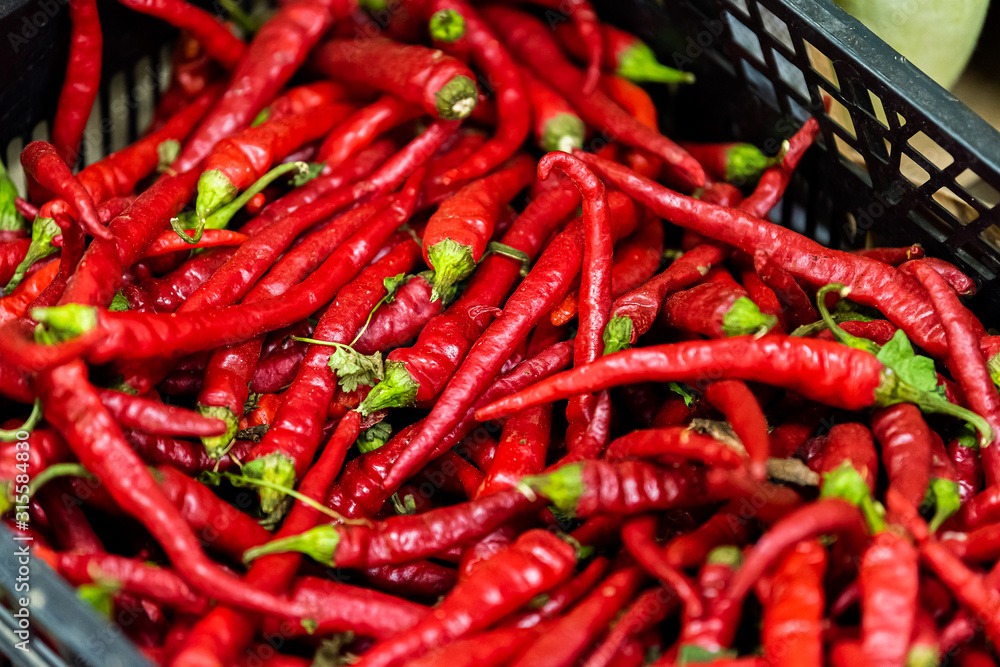 Closeup of many small raw vibrant colorful red color hot chili peppers in plastic crate box stall on display at farmers market in Florence, Italy Closeup of many small raw vibrant colorful red color hot chili peppers in plastic crate box stall on display at farmers market in Florence, Italy