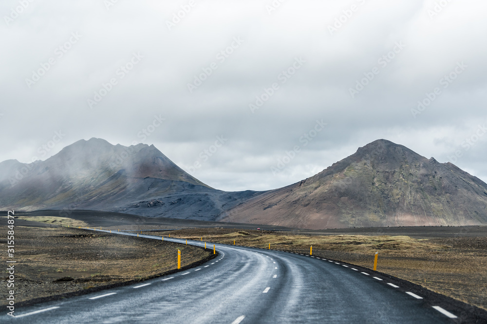 Fototapeta premium Ring road in east Iceland route 1 highway with barren bare brown landscape and rocky steep slope cliff with overcast cloudy stormy bad weather