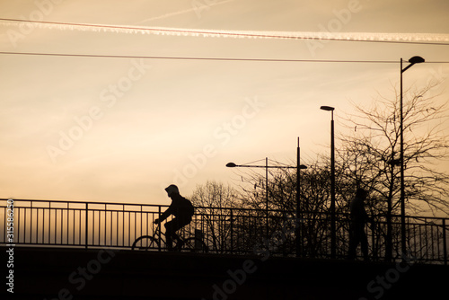 Silhouette of man with bicycle on bridge under the river by sunset
