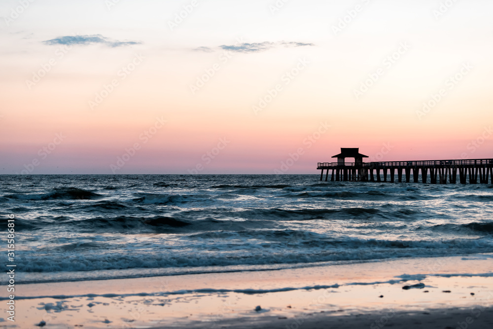 Naples, Florida colorful pastel twilight sunset in gulf of Mexico with pier wooden jetty silhouette with horizon and ocean waves