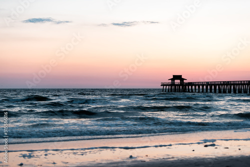 Naples, Florida colorful pastel twilight sunset in gulf of Mexico with pier wooden jetty silhouette with horizon and ocean waves © Kristina Blokhin