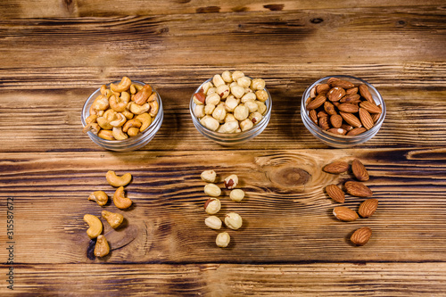 Various nuts (almond, cashew, hazelnut) in glass bowls on a wooden table. Vegetarian meal. Healthy eating concept