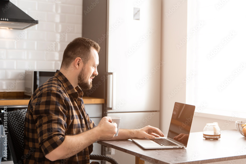 Guy with a cup of coffee is working on a laptop.