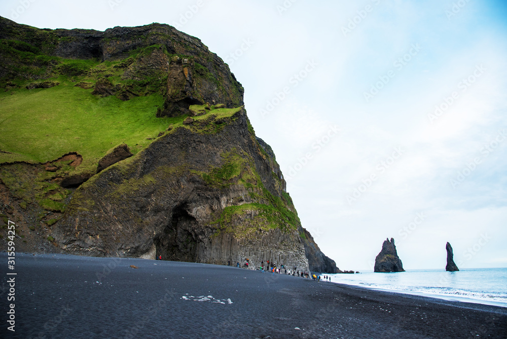Beautiful dramatic landscape with cave in basalt rock on the black sand beach on Reynisdrangar Sea Cliffs, stones called Troll under the Reynisfjall Mountain near Vik, Iceland. Exotic countries.
