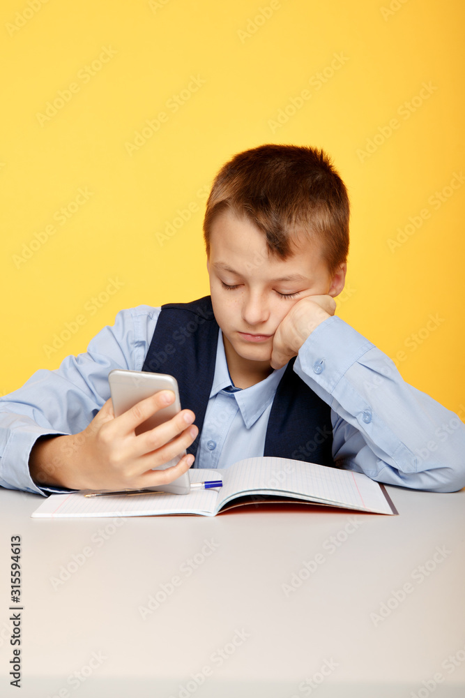Bored boy pupil watching phone at the lesson in the yellow classroom Bored boy pupil watching phone at the lesson in the yellow classroom