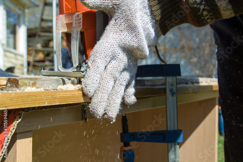 Woodworker cutting piece of wood using electric jigsaw in summer ootdoor photo