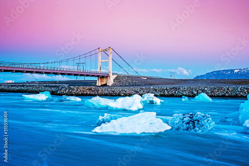 Obraz na płótnie Iceberg parts float to the ocean under a bridge in the bay in the famous Jokulsarlon ice lagoon in Iceland. (global warming, greenhouse effect - concept) w salonie