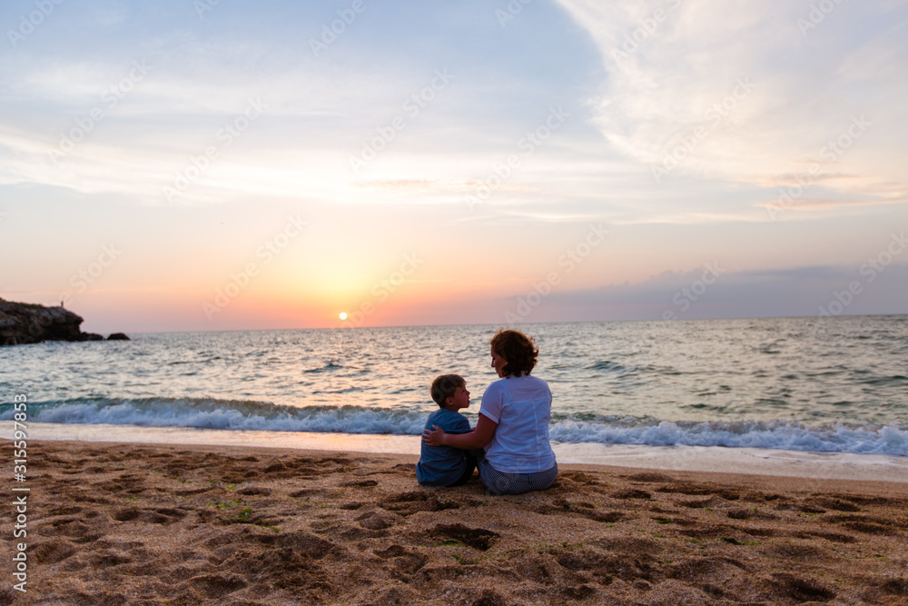 summer vacation. family mother and son sit on the ocean at sunset and look at each other