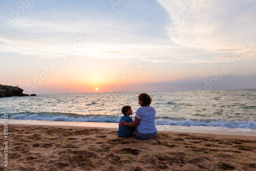 summer vacation. family mother and son sit on the ocean at sunset and look at each other