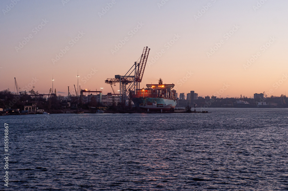 24-hour seaport work on loading container ships with cranes. Loading a large ship in the port at sunset. 24-hour seaport work on loading container ships with cranes. Loading a large ship in the port at sunset.