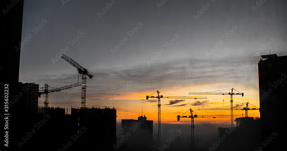 Building Construction With Cranes During Sunset. Cranes Building Construction Site At Sunset Or Sunrise. Silhouette Of Construction Tower Cranes In Sunset Sky Background.