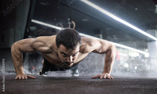 Sport. Handsome man doing push ups exercise with one hand in fitness gym. 