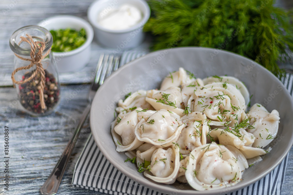 Boiled dumplings decorated with onions and peppers. In the background are greens, red peppers and bay leaves. On a light wooden background. Boiled dumplings decorated with onions and peppers. In the background are greens, red peppers and bay leaves. On a light wooden background.
