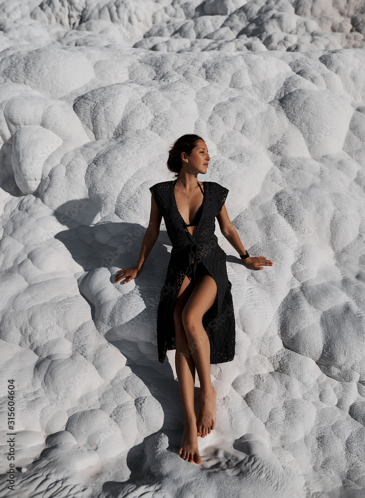 Young beautiful girl in black dress standing at natural pool Pamukkale. Natural travertine pools and terraces in Pamukkale, Turkey Young beautiful girl in black dress standing at natural pool Pamukkale. Natural travertine pools and terraces in Pamukkale, Turkey