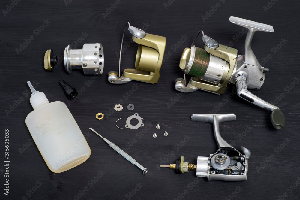 A fishing spinning reel as a whole and a second similar completely disassembled on a dark wooden background. Top view. A fishing spinning reel as a whole and a second similar completely disassembled on a dark wooden background. Top view.