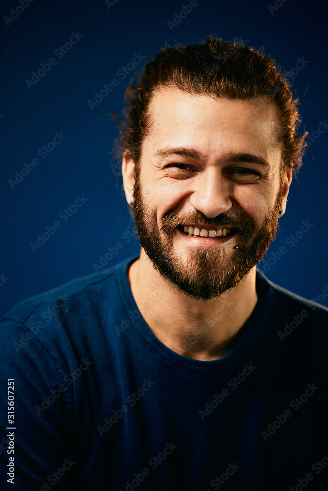 Portrait of pretty smiling bearded hipster posing in front of blue background and looking at camera.