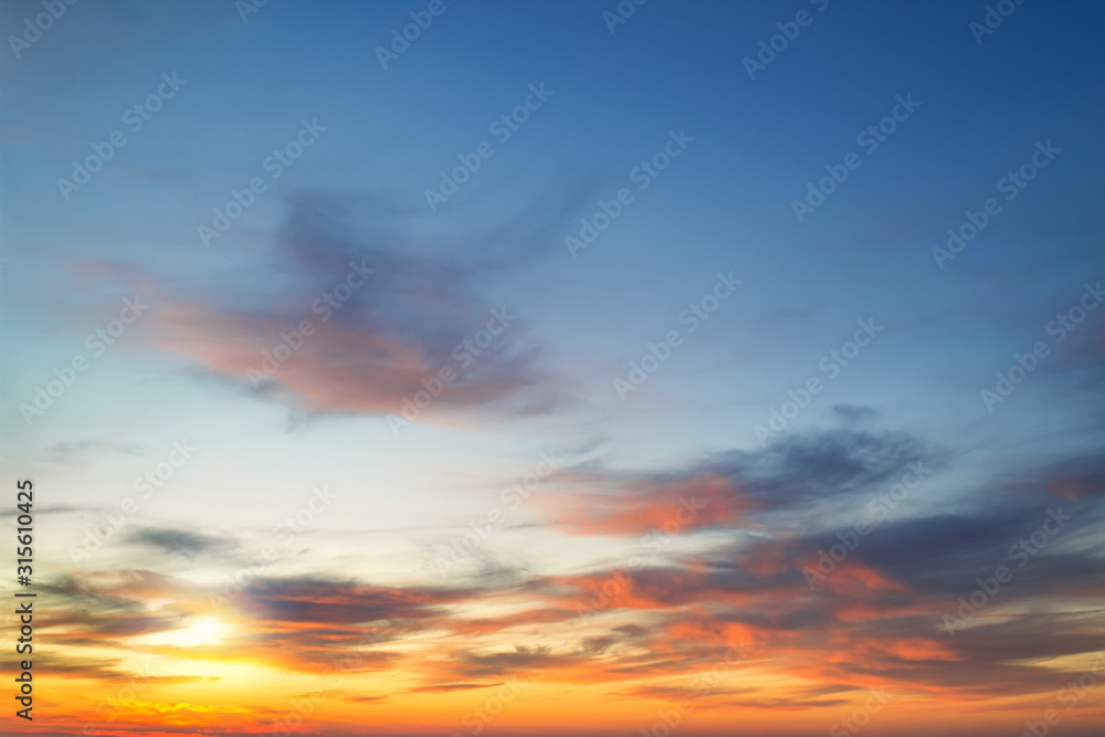 The setting sun shines through light clouds and paintes them with golden orange colors. Scenic skyscape at the sunset.
