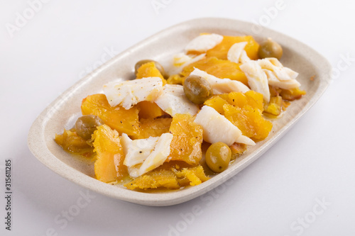 cod fish with sweet potato and olives on dish on gray paper background