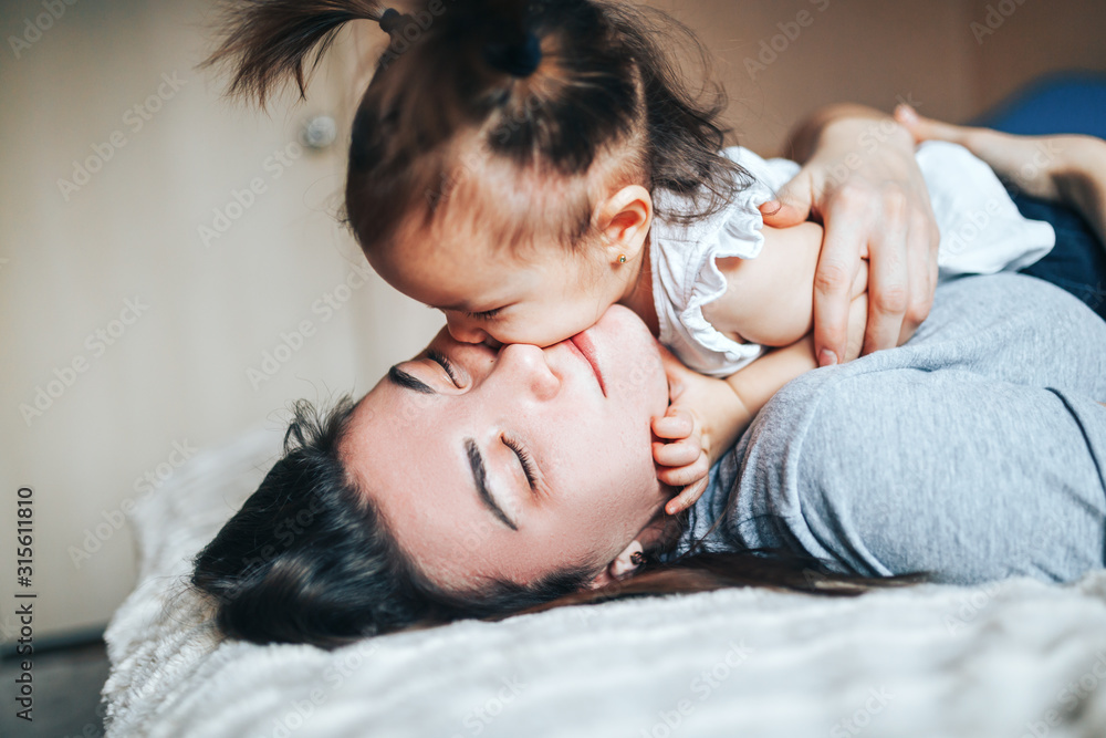 Lifestyle photo of young mother and small baby girl, hugging and kissing at home. Lifestyle photo of young mother and small baby girl, hugging and kissing at home.