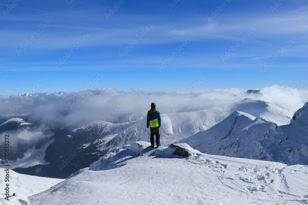 Magical panorama on peak of Chopok with view to High Tatras and Dumbier. Young skier enjoy freedom and paradise looks. Man in colorful ski clothes stand on the edge of mountain and watchs landscape