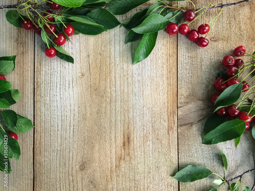 Fresh sweet cherries with leaves on wooden background, top view.