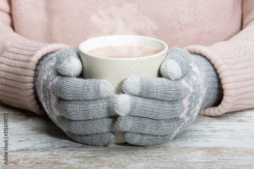 Hands in warm gloves hold a cup with a hot cocoa drink, tea or chocolate. Close-up. Rest during winter sports