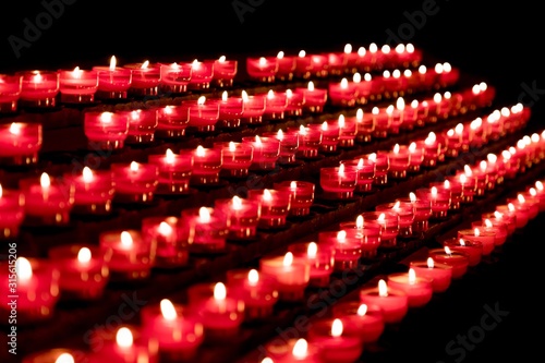 Group of red candles in church for faith resurrection prayer. Candlelight fire flames in rows are silent religion symbol for peace, life and soul. Obituary hope sacrifice against sorrows and pain