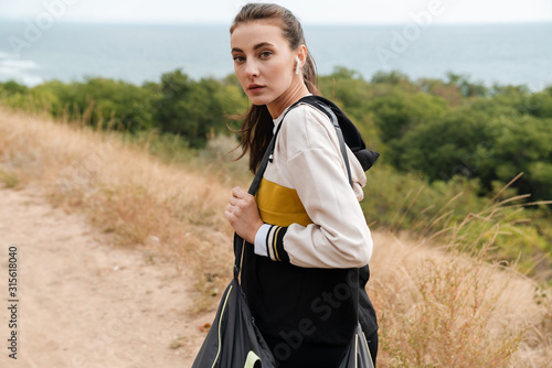 Photo of nice brunette woman using earpods while working with bag