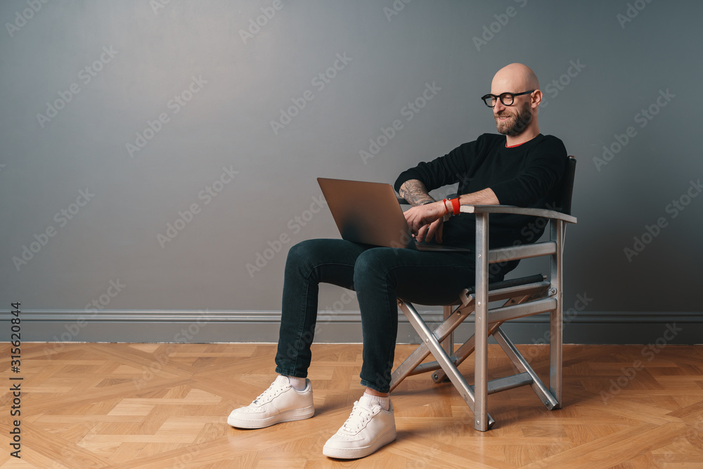 Modern young caucasian man with beard and glasses relaxing while surfing internet on laptop pc