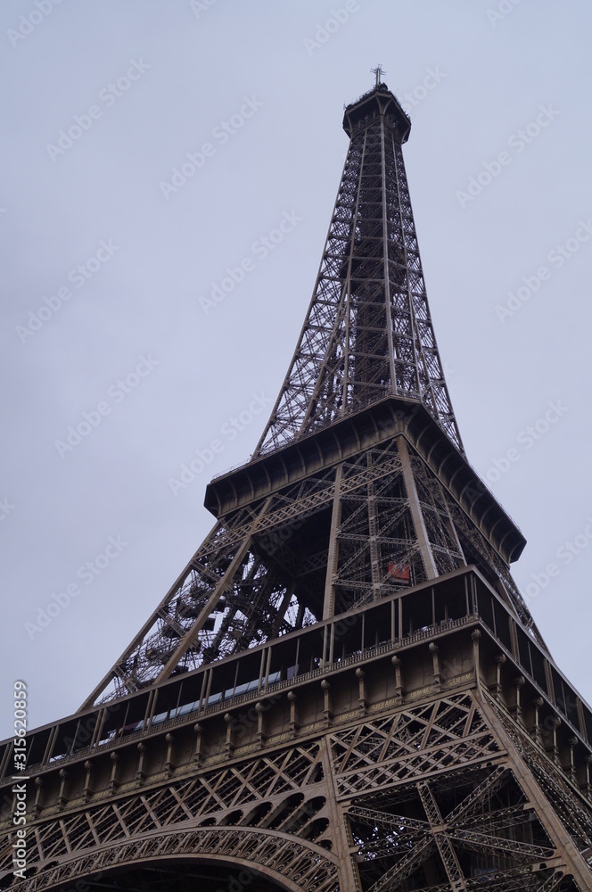 Vista de la Torre Eiffel desde el suelo donde se aprecia su altura junto a un cielo azul y nublado